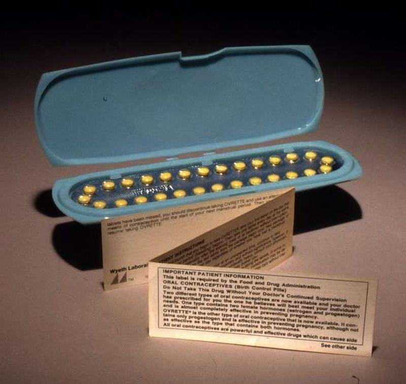 A vintage package of of birth control pills in a blister package that is inside a rectangle blue plastic package. In front of the package is a three-fold list of instructions for taking them. The list is standing up.