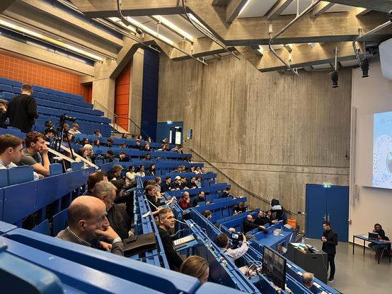 Hörsaal, steile blaue Sitzreihen, Wände orange, Decke mit Sichtbeton-Ornamenten 