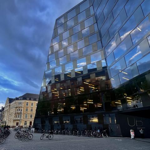 Fassade der UB Freiburg mit sehr vielen Fenstern, in denen sich dunkle Wolken spiegeln.