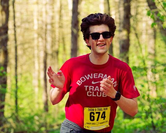 Man with dark classes, moderately short hair and red shirt running in the woods