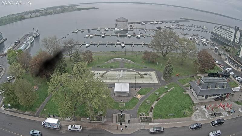 Looking SE from the City Hall clock tower looking out over Ontario Street, Confederation Park and the marina, the Shoal Tower and where the Cataraqui River meets Lake Ontario. // Image captured at: 2026-05-19 13:00:02 UTC (about 1 min. prior to this post) // Image sourced from: cityofkingston.ca // Current Temp in Kingston: 58 F | 14 C // Precip: broken clouds // Wind: SSE at 6 mph | 9 kph // Humidity: 94%