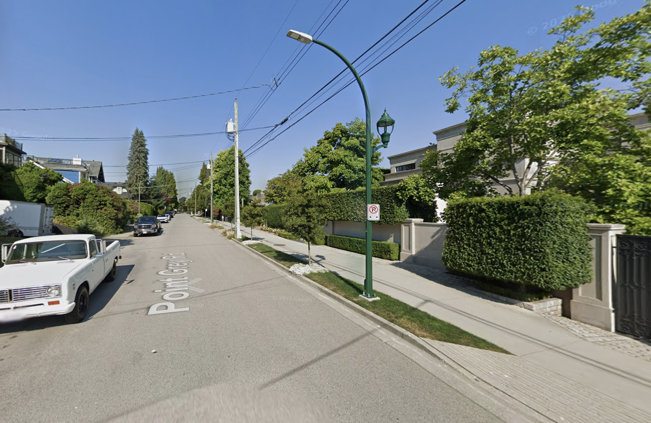 A residential street lined with houses with pretty landscaping, a few cars parked on the street, no bike lanes in sight