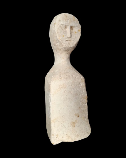 A figurine carved from white stone, depicting a simple face, long neck, and featureless body.