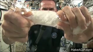 ein Astronaut auf der ISS wringt ein nasses Stück Stoff aus - das Wasser sammelt sich in der Schwerelosigkeit rund um die Stoff
