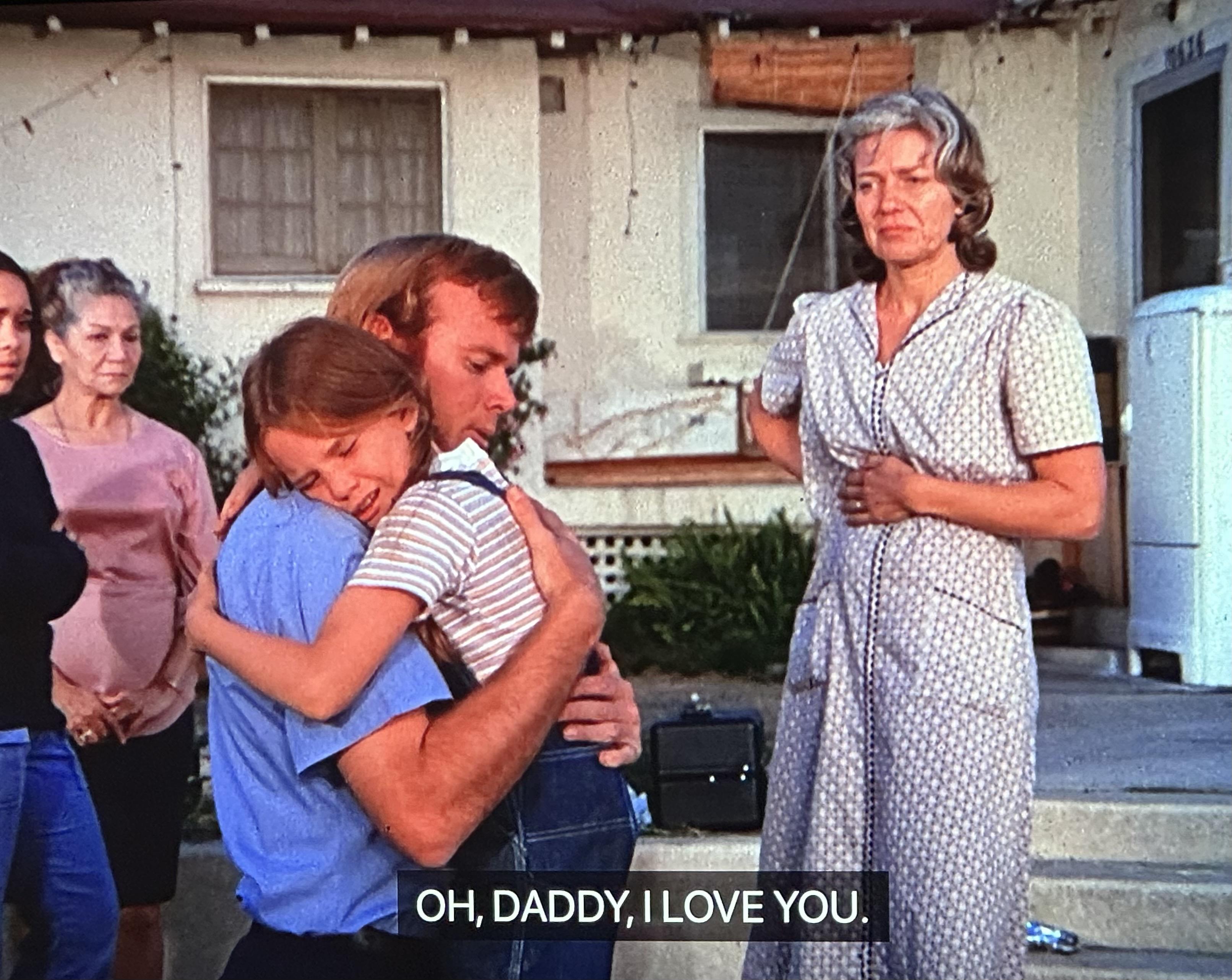 A very young girl played by actress Melissa Gilbert hugs, fireman De Soto as her mother looks on