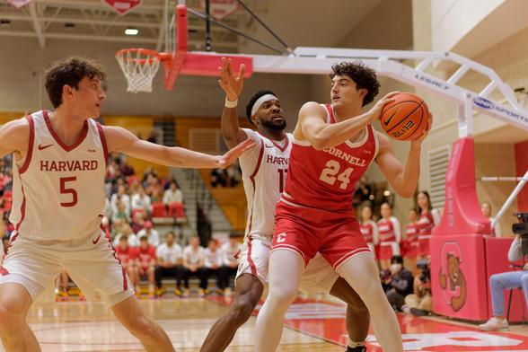 In front of the basketball net and structure that holds up find red 24 a white guy holding a basketball with a black guy right behind him and a white guy on the left side of the frame