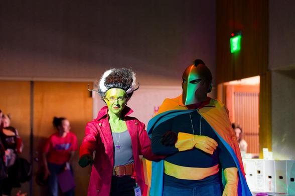 Green-faced woman walks on ITHACON cosplay runway with a man wearing a helmet