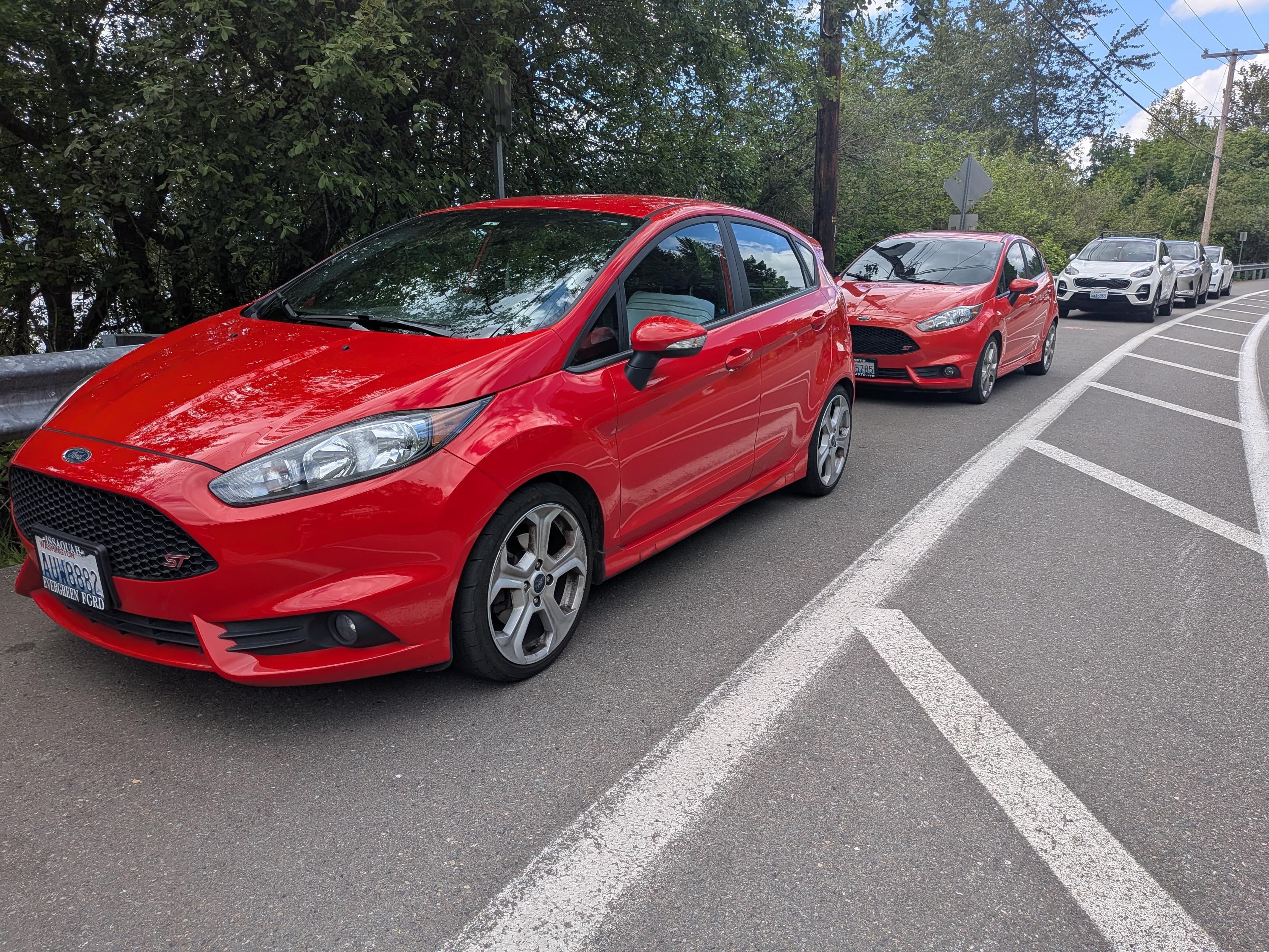 Two red Ford Fiesta ST hatchbacks parked on the side of the road one behind the other. 
