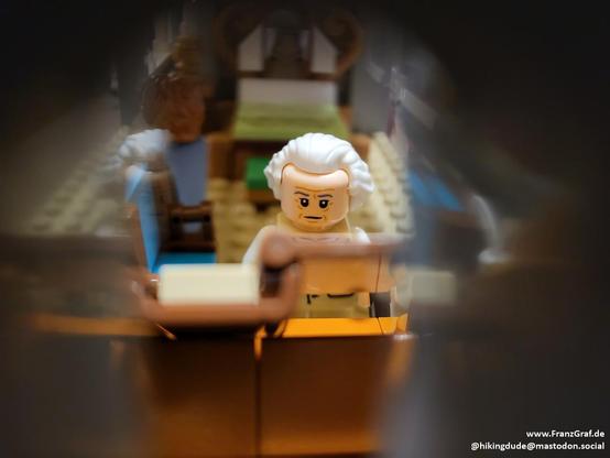 This image captures a playful and creative scene featuring a LEGO minifigure representing Bilbo Baggins in a detailed, miniature setting. The minifigure, dressed in a white outfit and cap, appears to be a chef or baker, holding a rolling pin. The figure is positioned in the foreground, drawing the viewer's attention with its expressive face and the intricate details of its attire and accessories.