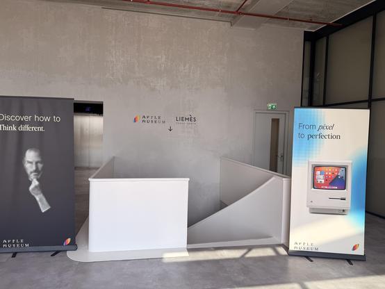 Zwei Werbetafeln für das Apple Museum in einem Raum mit Treppe und Aufzug.