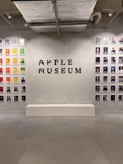Graue Wand mit "Apple Museum" Schriftzug, flankiert von bunten und schwarz-weißen Porträts von Personen.