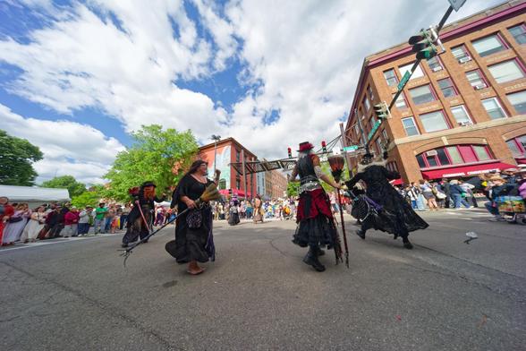 Several woman holding brooms dance in a circle with somewhat goth glothing