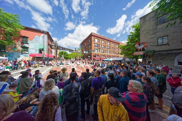 People surround a square with with-dressed danced surrounded by antique buildings under a blue sky with white cumulus clouds