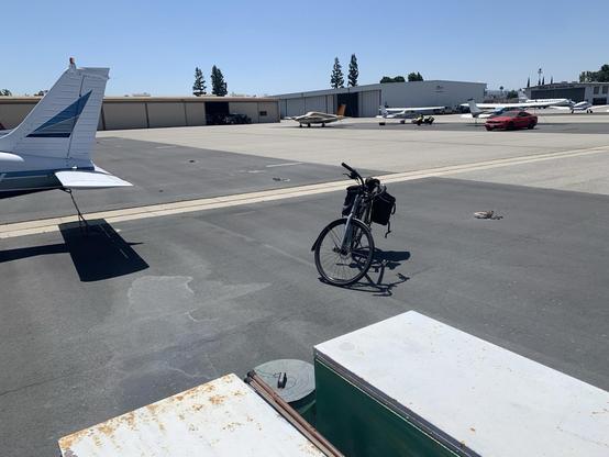 A wider fire of the scene showing the chain, egg, and bird, along with a bicycle and several parked airplanes on a broad expanse of pavement