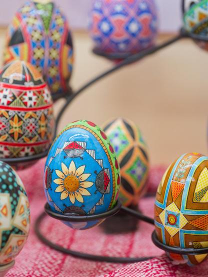 A spiral of colorful eggs in the background around a blue egg with a yellow flower and triangular decorations.