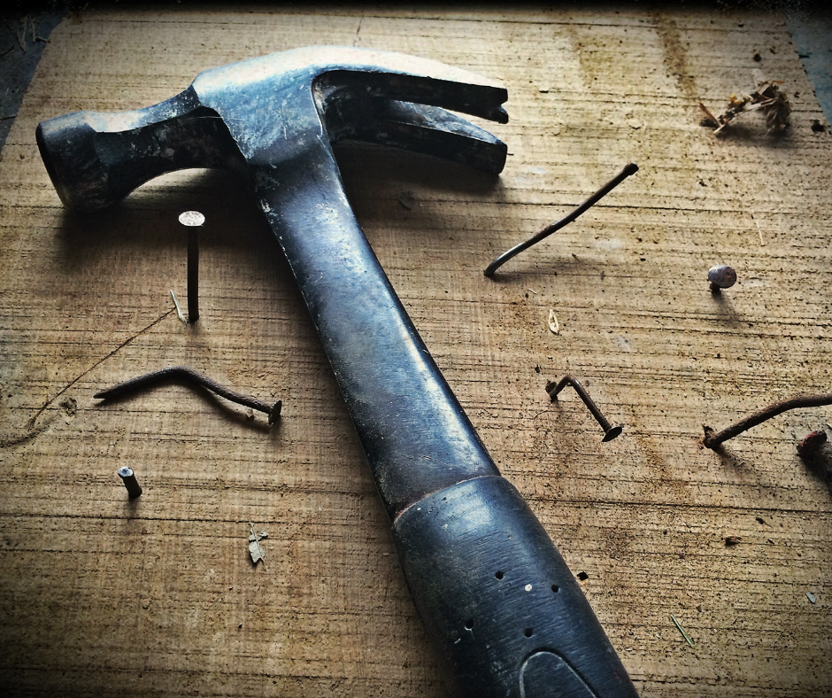 Hammer sits on a workbench with a lot of nails surrounding it (some of them bent)