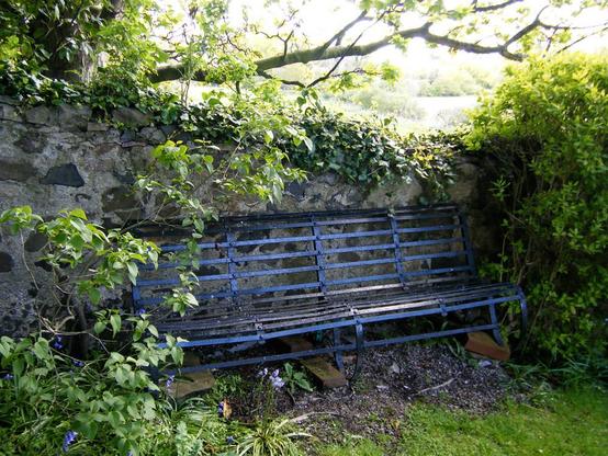 A vintage blue bench placed against a stone wall in a lush garden. Edinburgh.