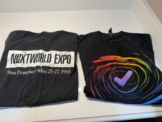 A photo of two T-shirts. The first is from NeXTWORLD Expo 1993, the first conference I ever traveled out of town to attend. The second is from last year's Liquid Glass update to OmniFocus.