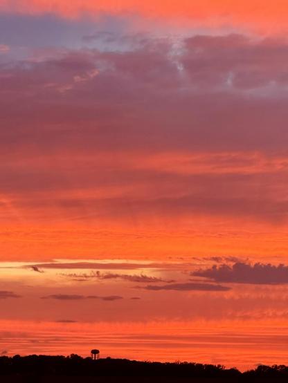 A bright orange reflection off the clouds and a distant water tower