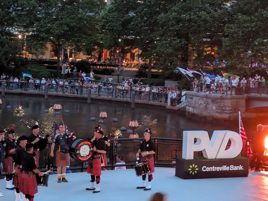 Tartan Army bagpipe band (in kilts), PVD sign, Waterfire visible behind