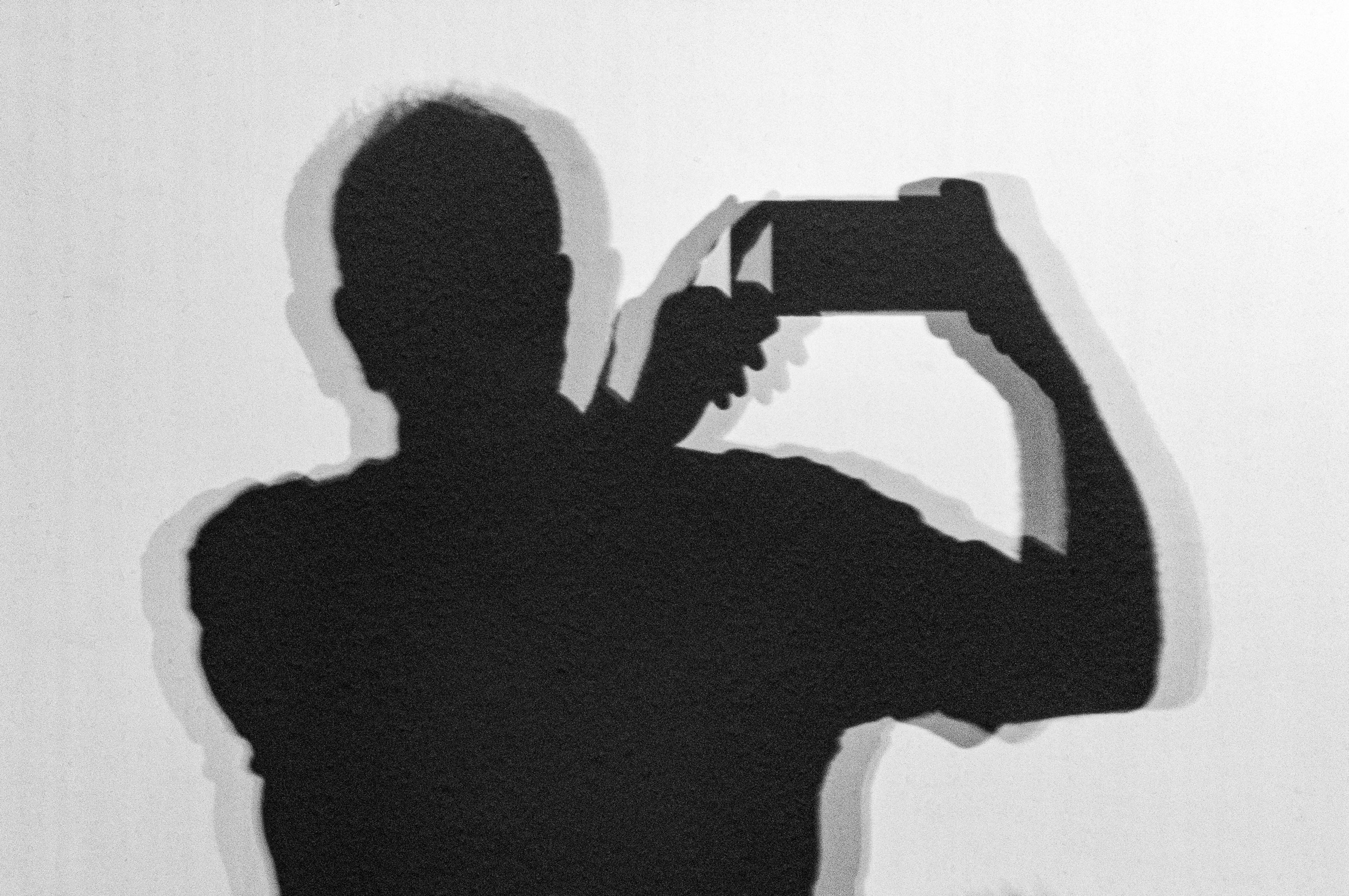 A picture showing my shadow cast on a white wall. I’m holding my phone up to one side to take the picture, and the shadow is double because there are two sources of illumination. Where they overlap, the combined shadow is darker.