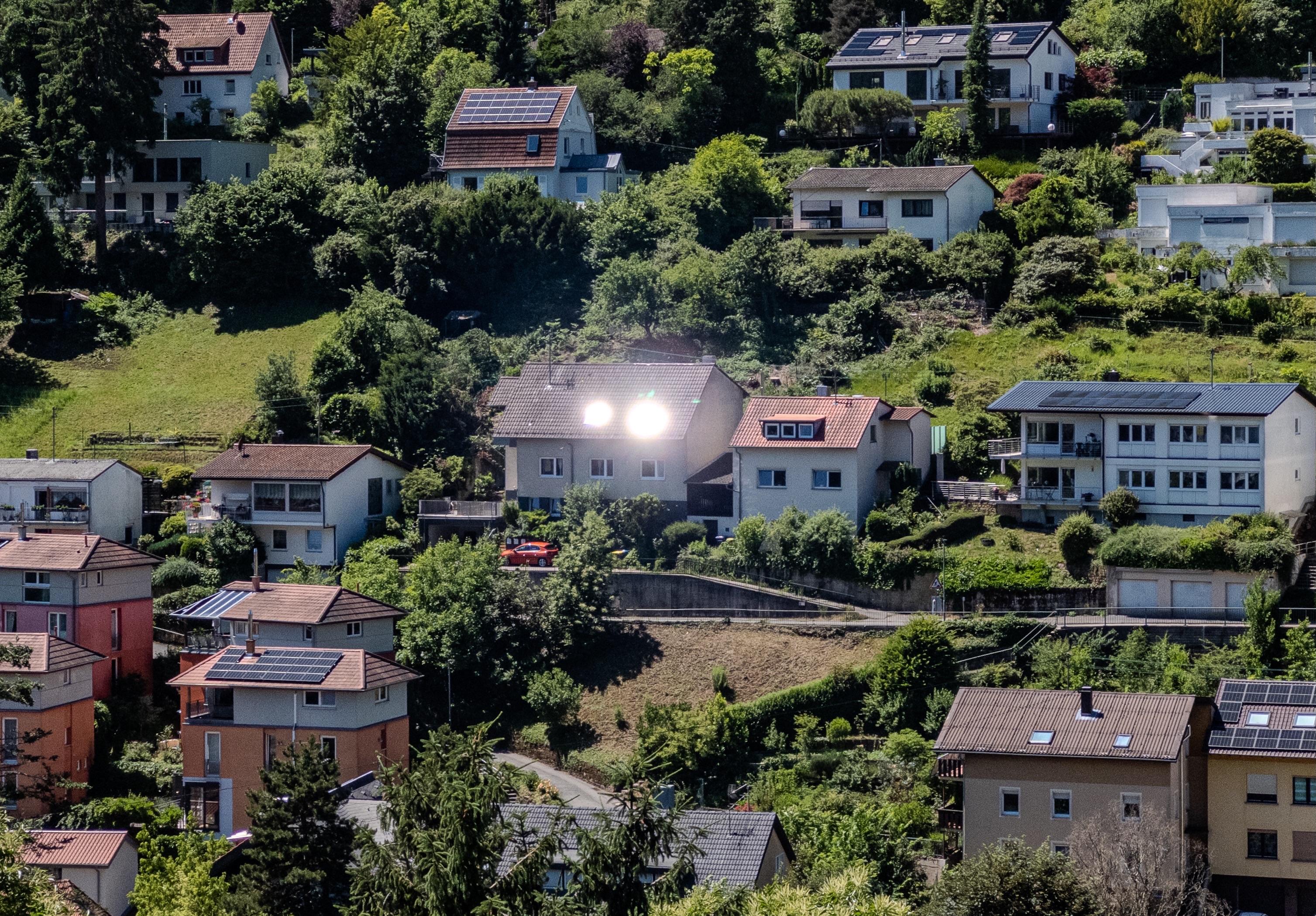 A picture looking across the valley at very houses, one of which has two bright spots of light where the Sun is being reflected from angles windows in its roof.