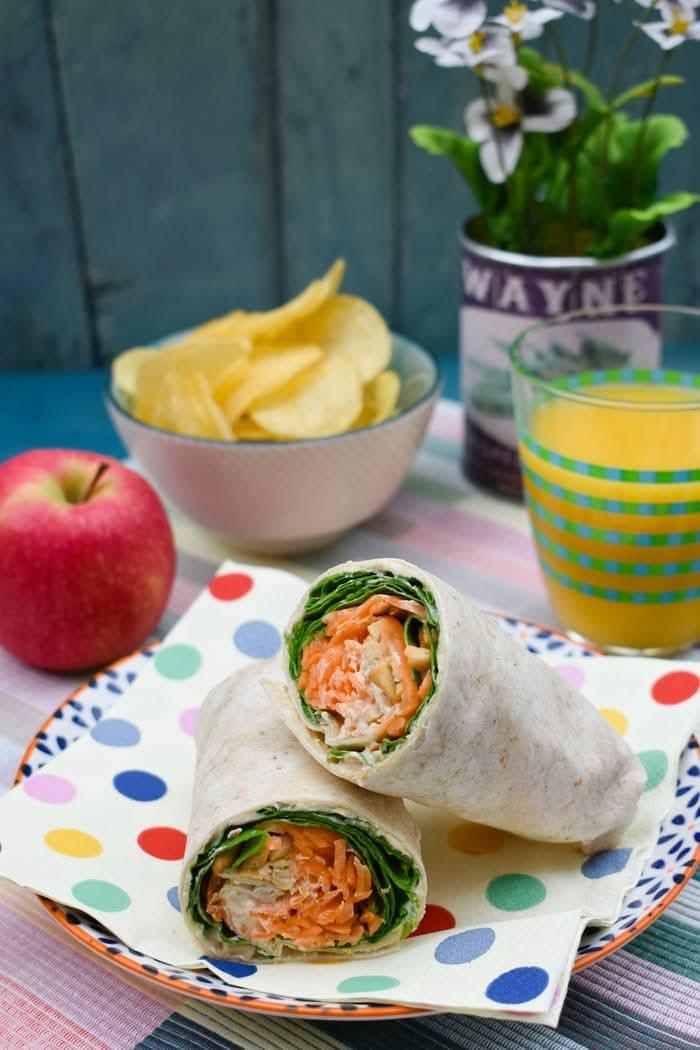 Carrot crunch wrap served with an apple some crisps (chips) and a glass of orange juice.