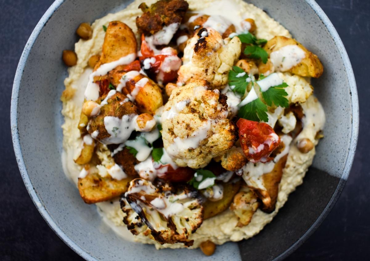 Lebanese Cauliflower & Potato Bake served in a bowl on a bed of garlicky hummus and a drizzle of tahini dressing.