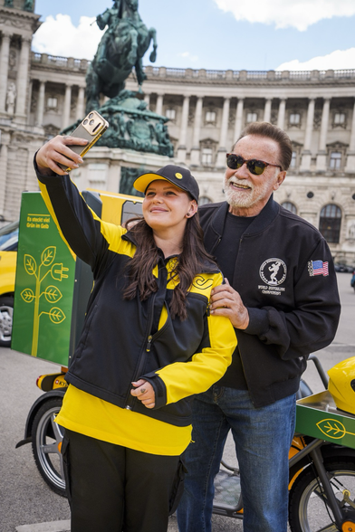 Person in postal service uniform taking a selfie with Arnold Schwarzenegger