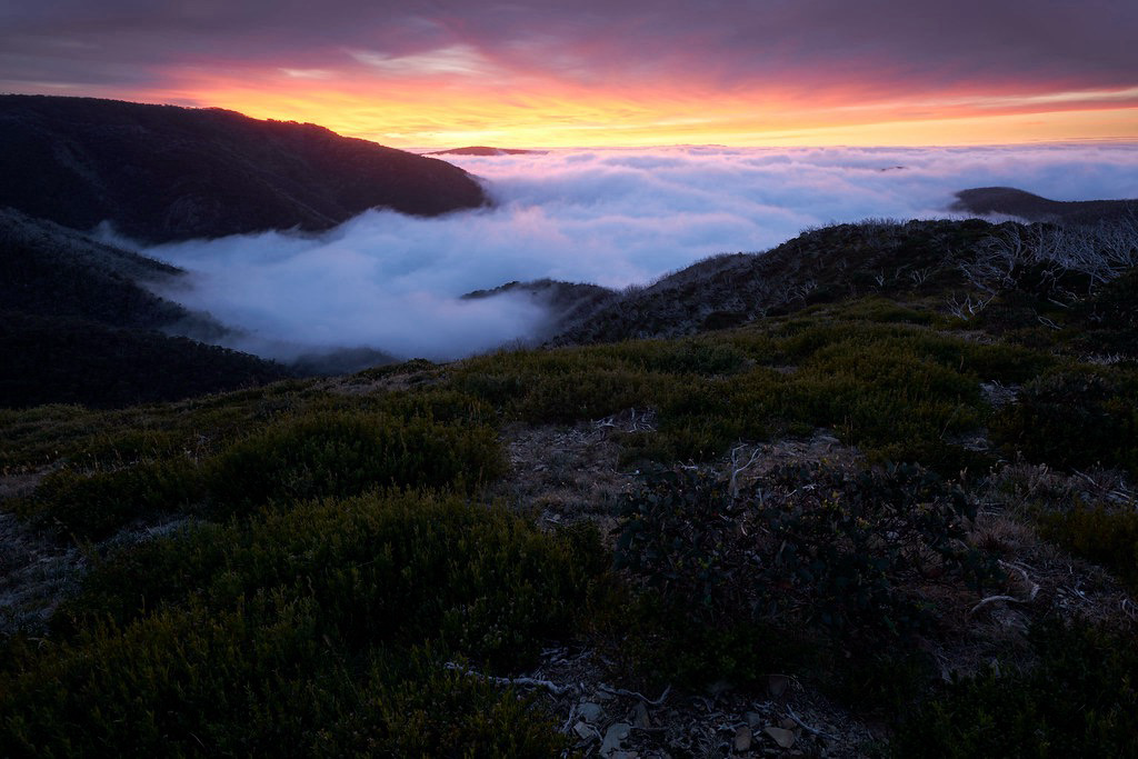 Sunrise with clouds in the valley below and above the mountains brightly lit with colours of sunrise.