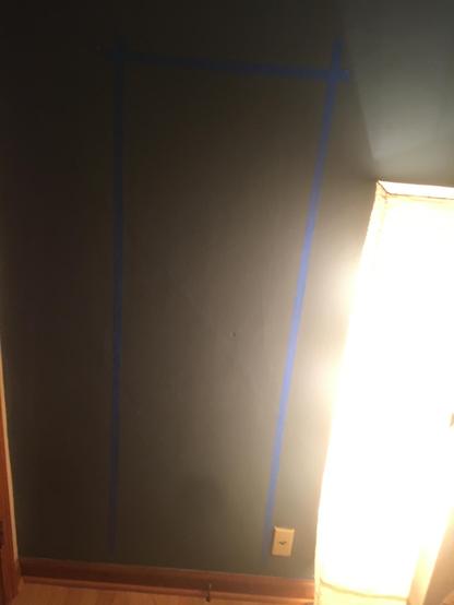 An image of a wall, with blue tape on it outlining a doorway that does not appear to be there.
