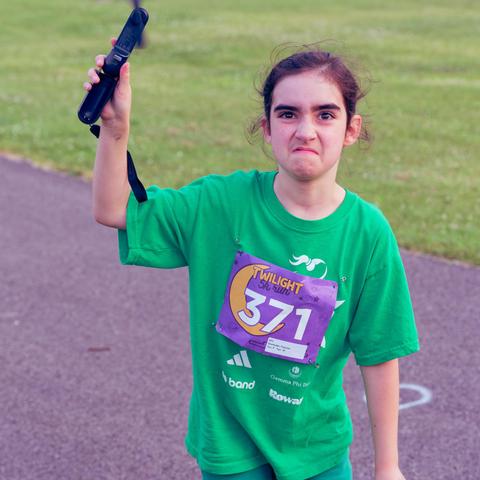 Child wearing green shirt holds a battery powered fan in one hand and has a grimace on her face