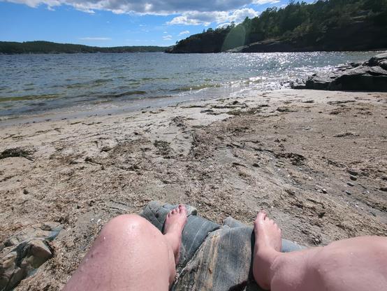 A view of a sunny beach and a couple of pale legs