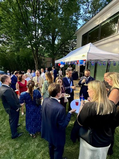 A party of people in a back yard with an event tent