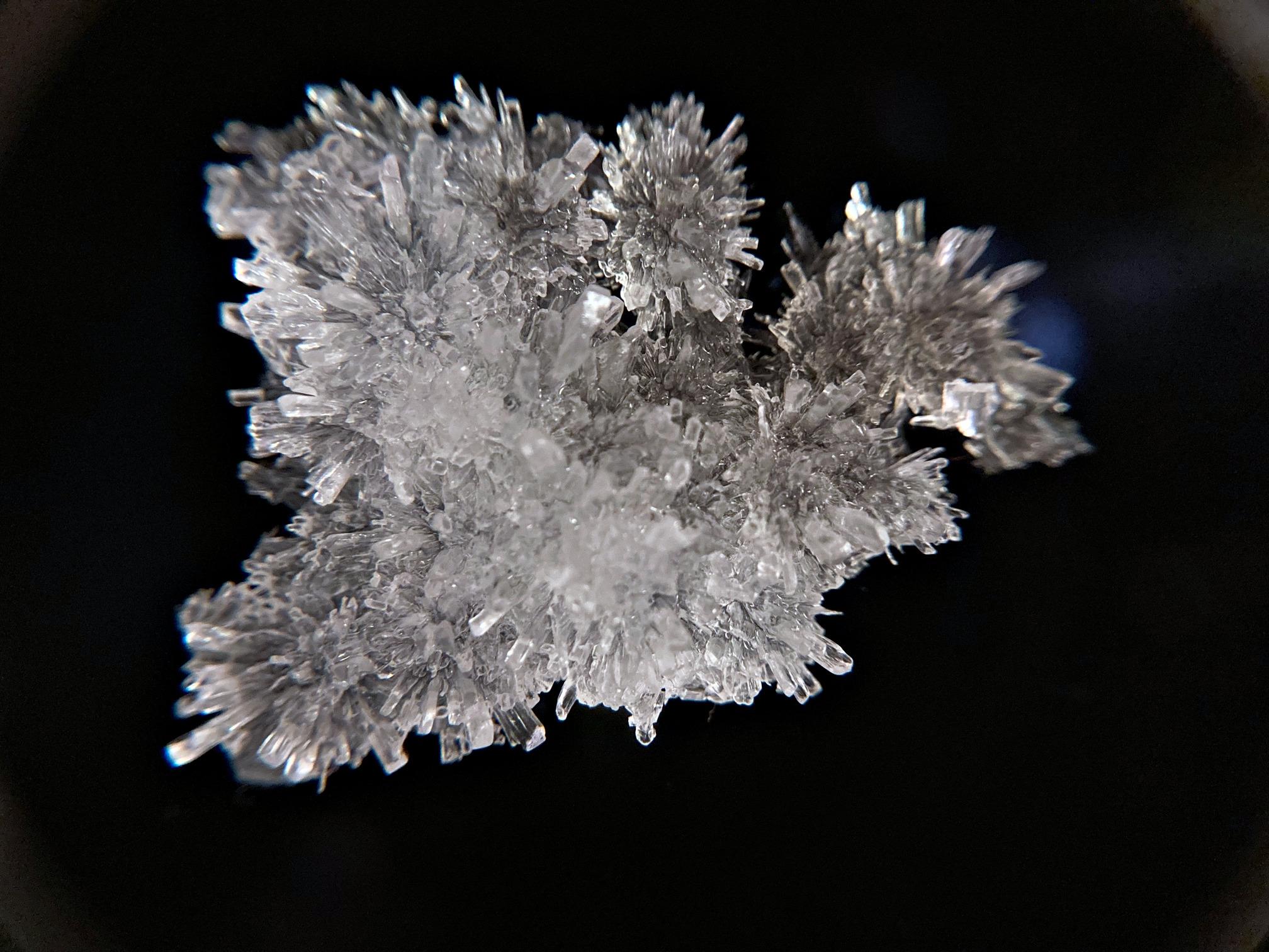 white-translucent crystal on black backdrop. "feathery", lacking for better vocabulary - not classically well-grown clean cube-shape