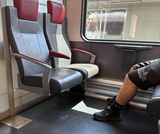 Sitzbank mit Ledersitzen in der S-Bahn. Gegenüberliegend sitzt eine Person. Man sieht nur die kurzbehosten Beine und Turnschuhe.