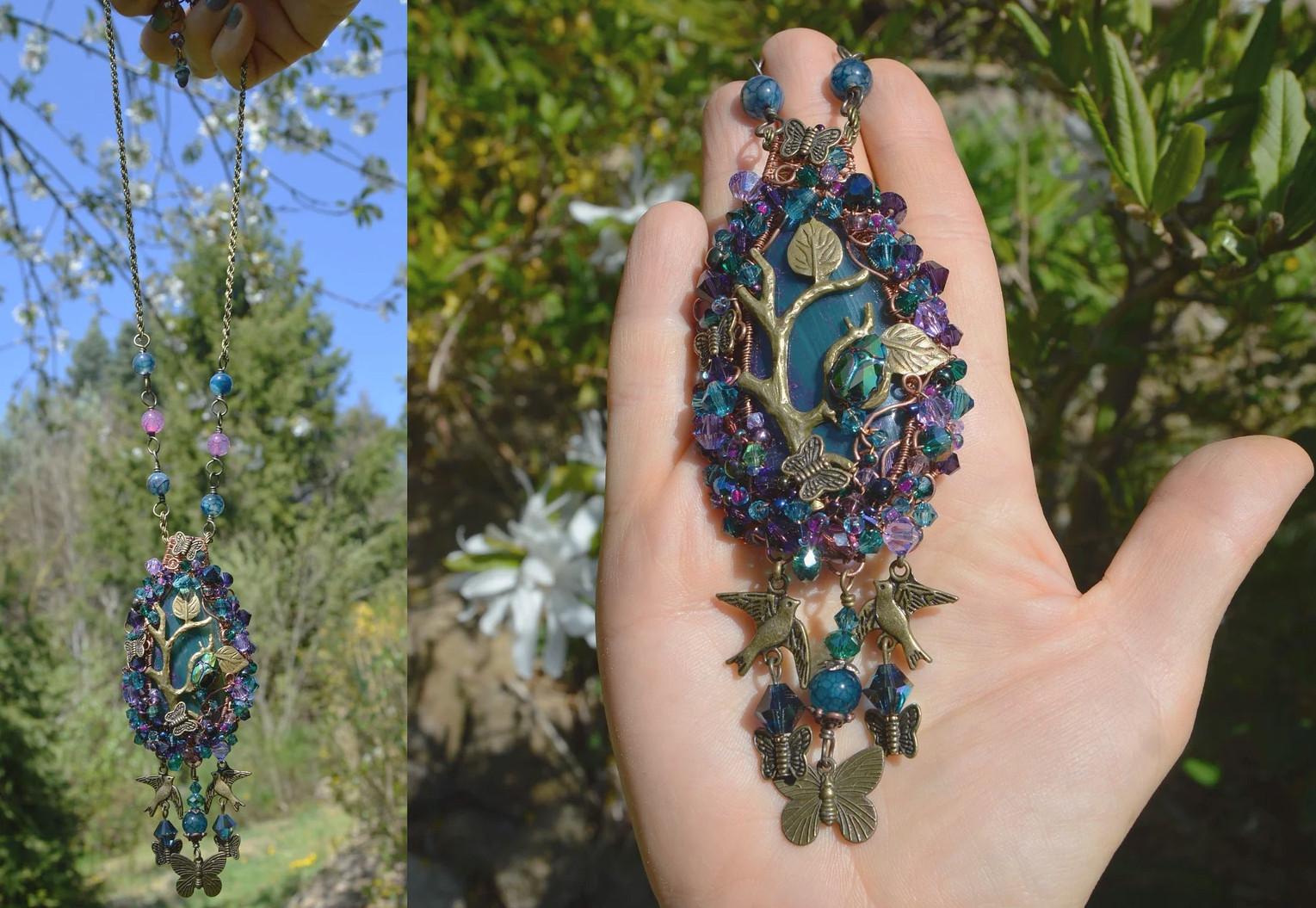 Elaborate pendant of woven green and purple beads and copper wire around a central green stone. Branches and leaves, small butterflies, and a crystal beetle are woven into the design. Left is the pendant hanging on its long chain against a background of trees and sky. Right it is held in the palm of a hand for scale.