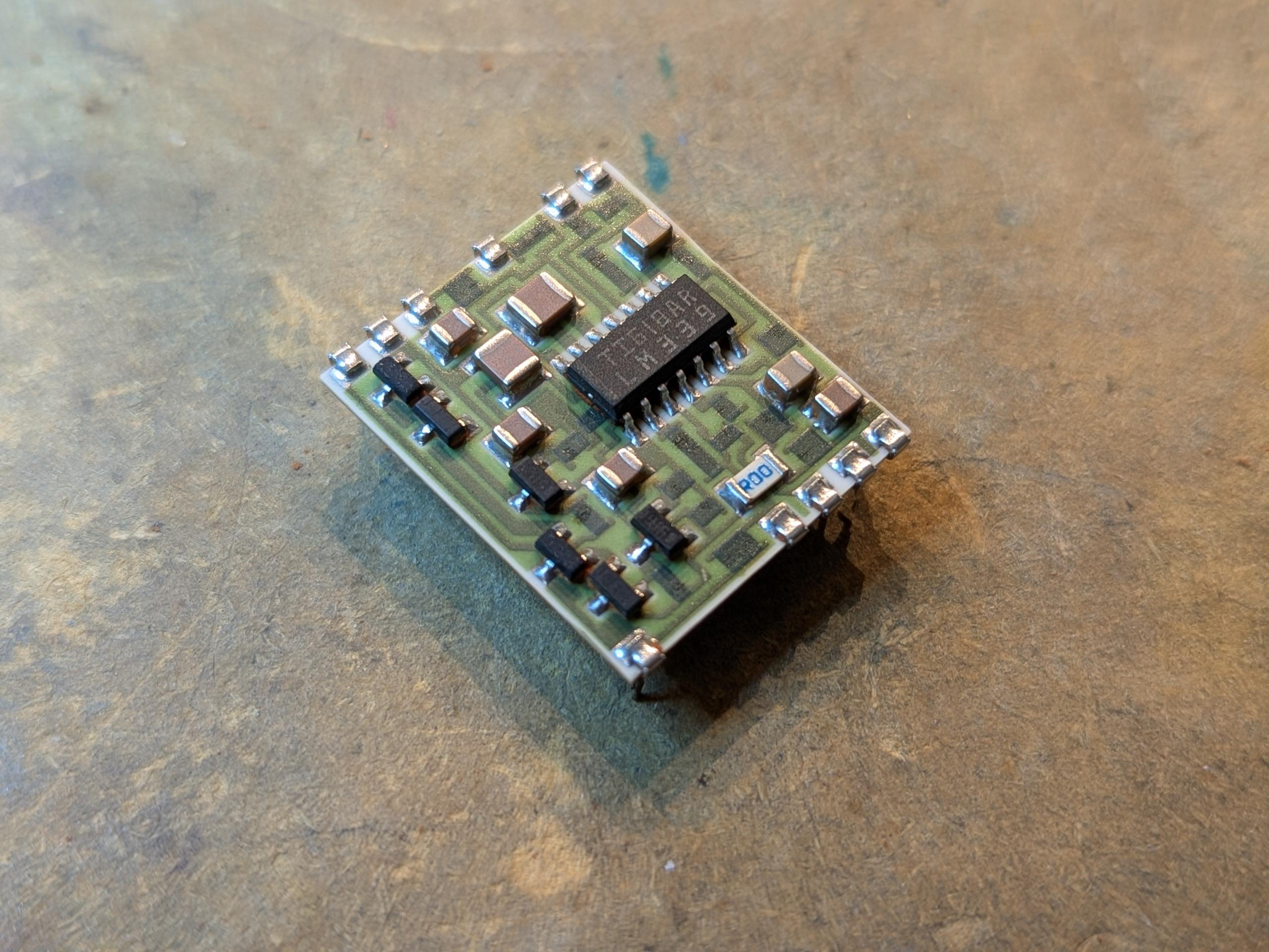 white ceramic board with light green mask and trace, with dark rectangles. clipped to the edge are some soldered pins.