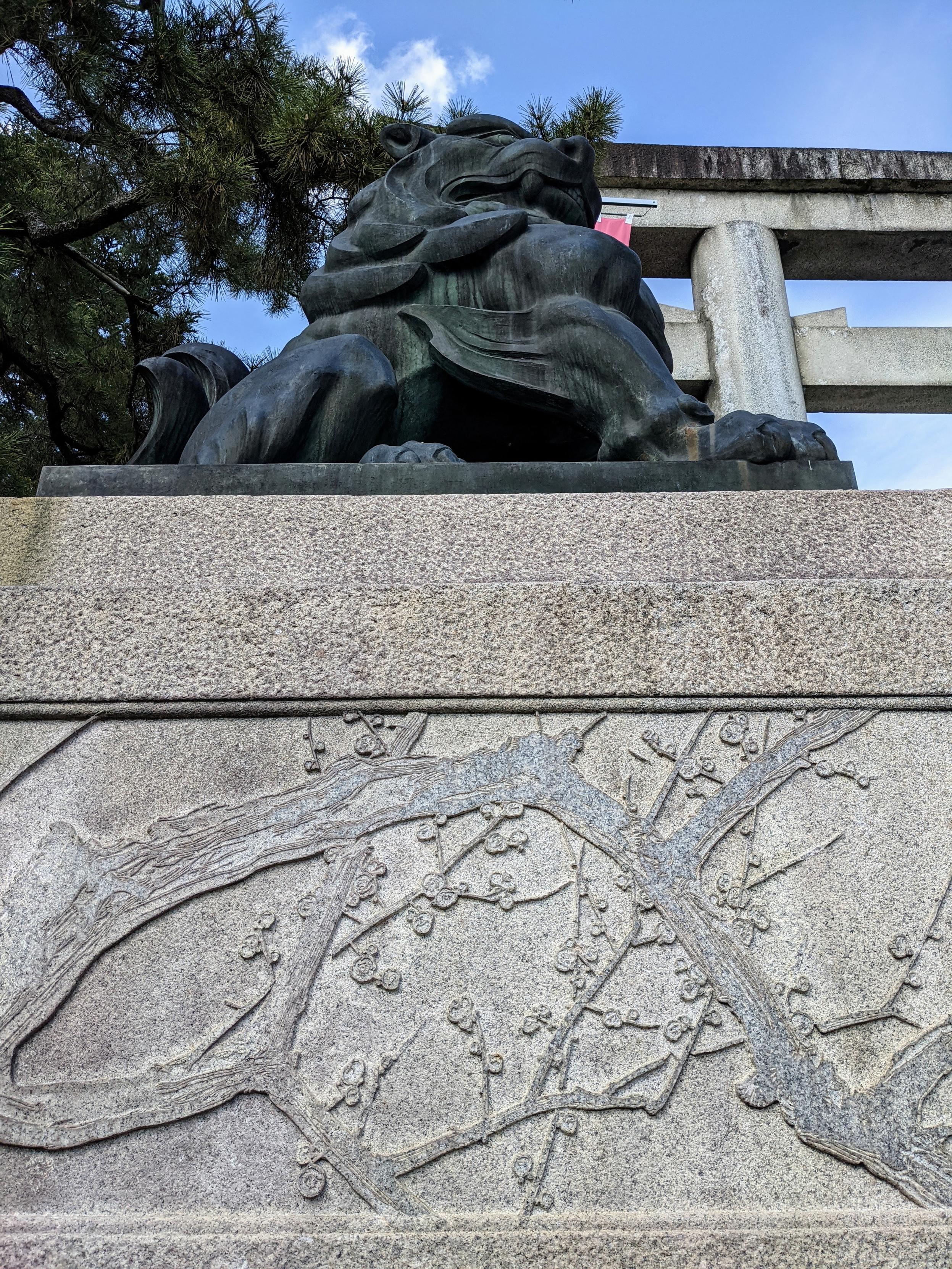 The stone plinth beneath the komainu at Kitano Tenmangu's main torii is carved with ume branches and blossoms.