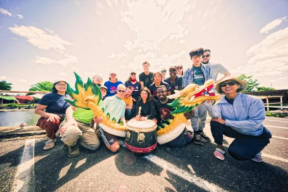 A whole lot of people gather around a drum flanked by two segments of a dragon under a blue sky that got blown out to white near the center of the frame