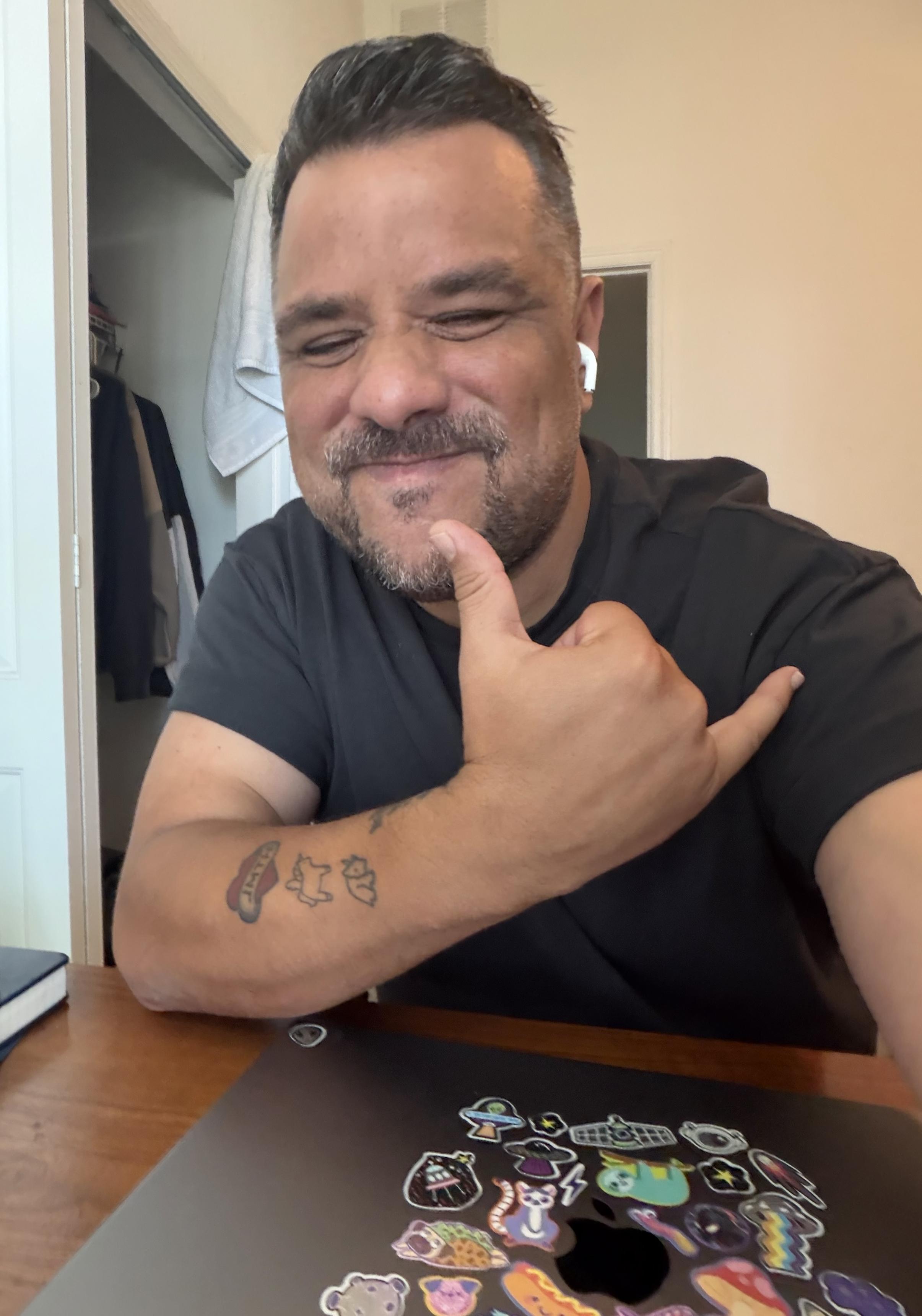 Me smiling with my eyes closed thumbs up. Wearing black shirt. Laptop in front of me. 
