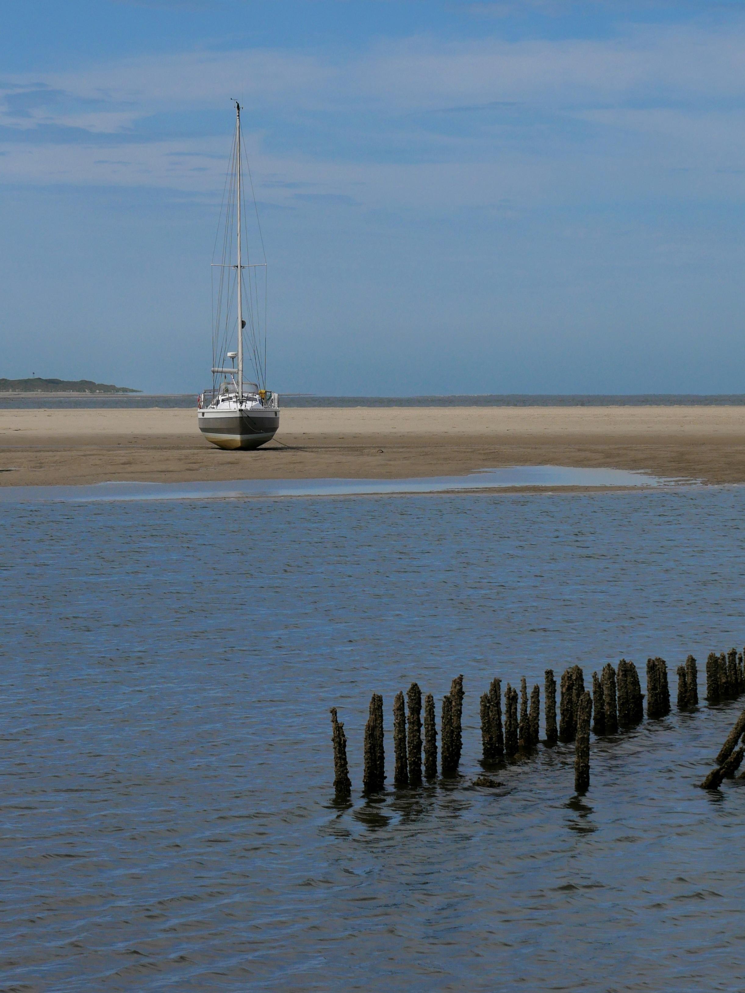 Eine Yacht am Westende der Insel Spiekeroog liegt auf dem Trockenen aufgrund der Ebbe. Im Vordergrund ist ein Priel zu sehen und im Hintergrund ein Stück der Nachbarinsel Langeoog. Spiekeroog 2026
