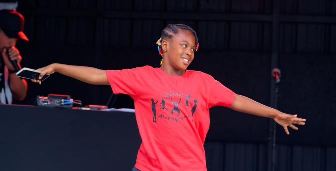 Young girl with red GIAC jumpers shirt dances with cell phone in one hand and DJ behind