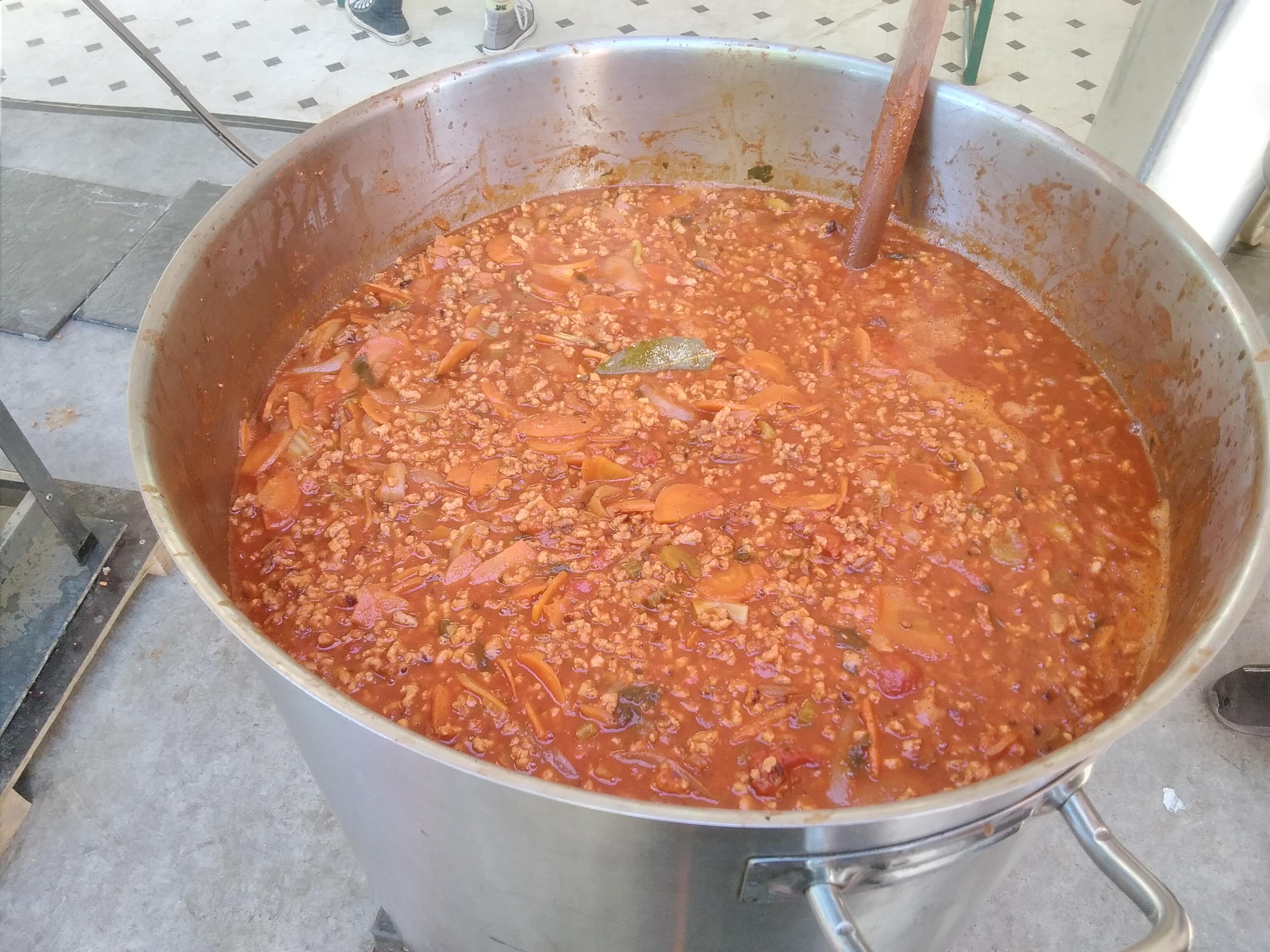 A 200-litre pot of vegan pasta sauce, almost full and with a huge wooden spoon in it.