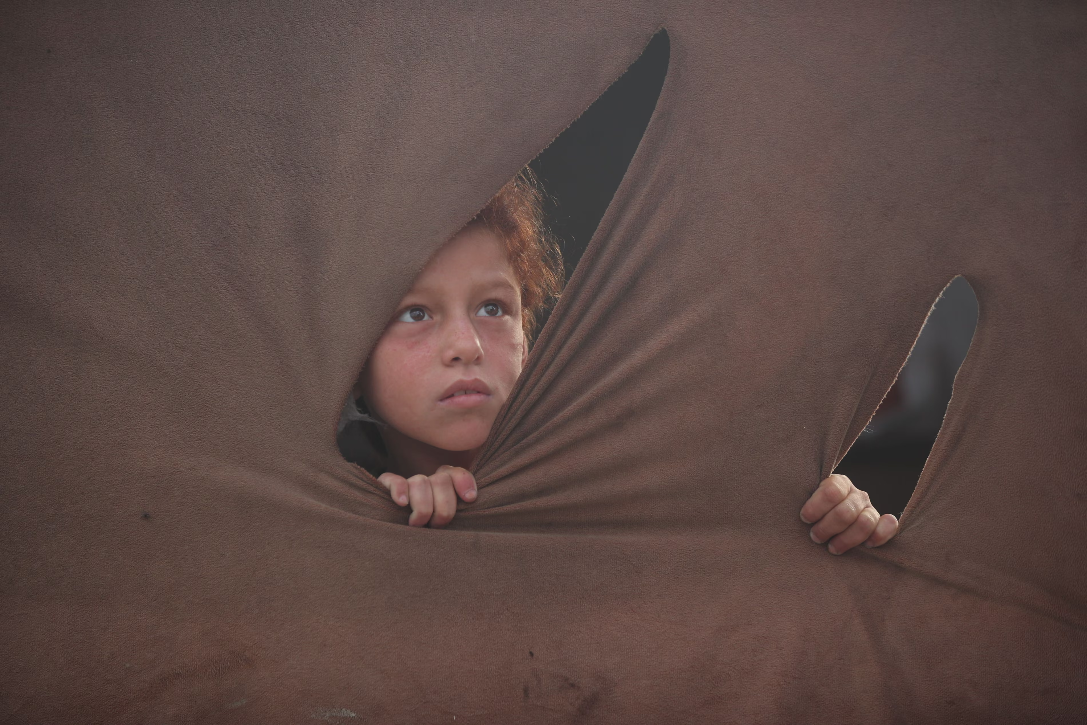 A displaced Palestinian girl looks through a hole in her family’s tent.