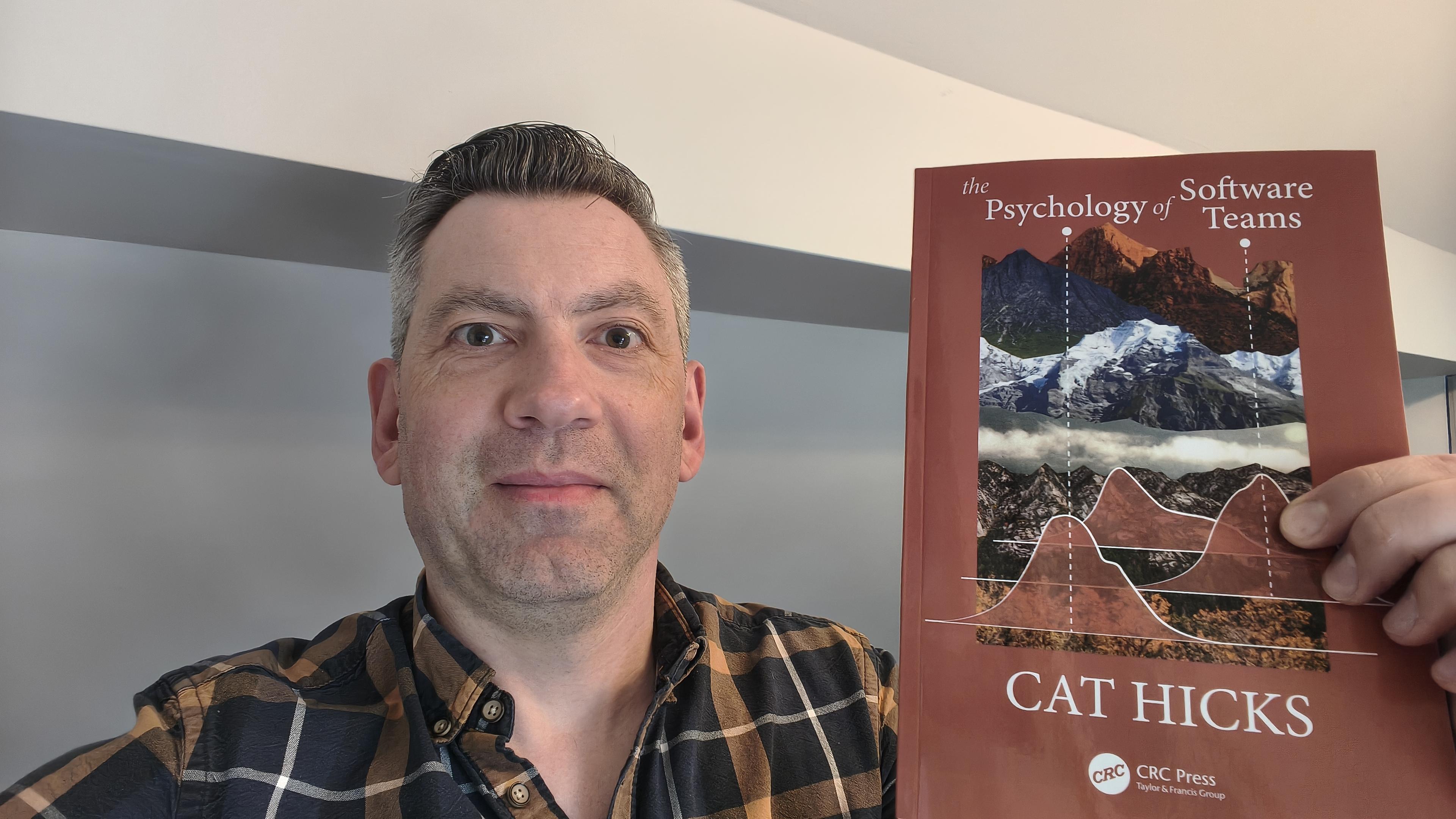 A guy holding up a book called The Psychology of Software Teams