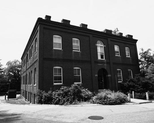 Monochrome image of a dark brick building in two point perspective under a grey sky