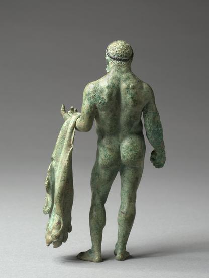 A bronze statuette of Herakles, seen from behind. The hero is in the nude, his lionskin over his left arm, in his right hand (presumably) the apples of the Hesperides.