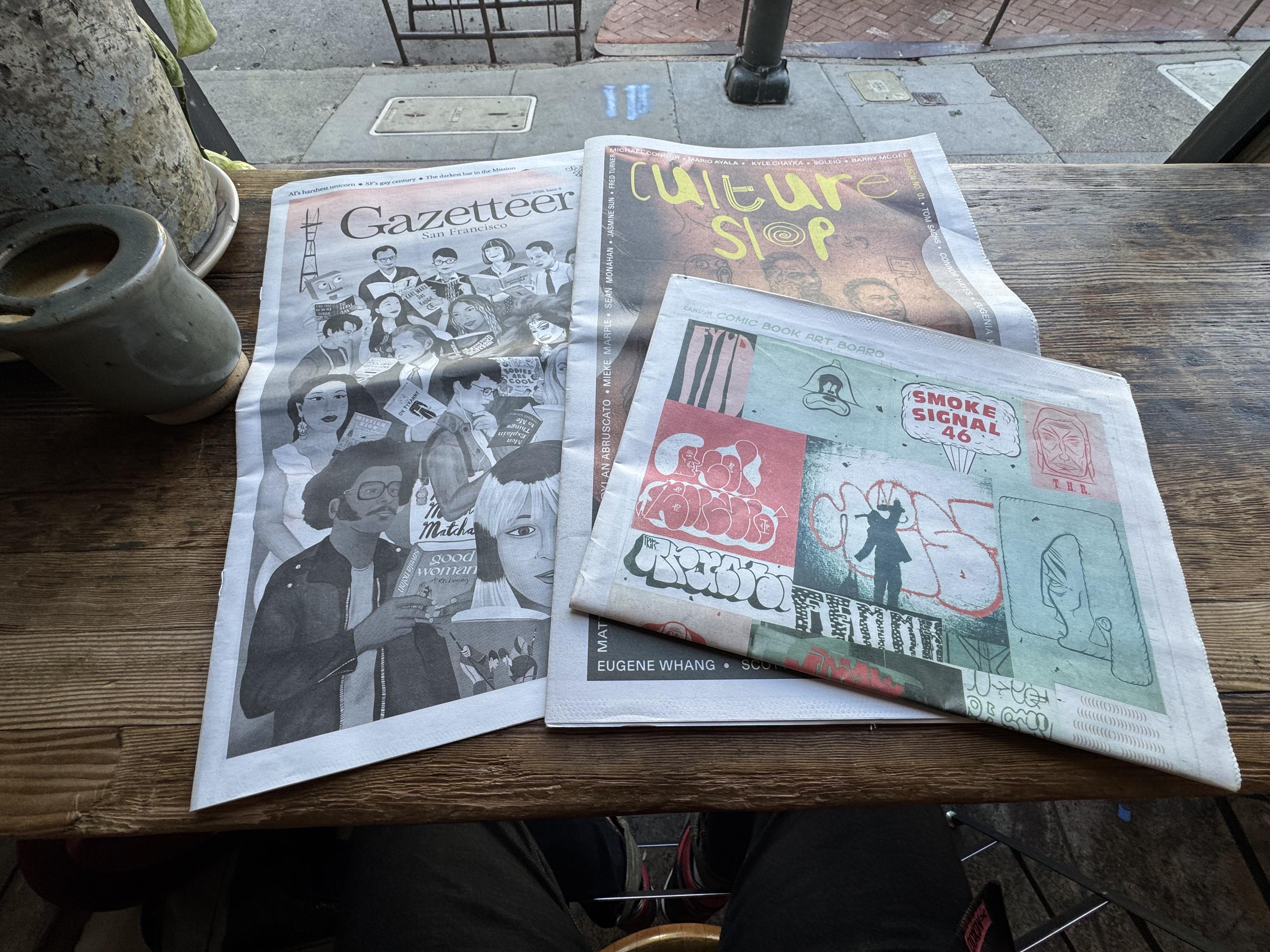 A photo of three different alternative newspapers: The Gazetteer, Culture Slop, and Smoke Signal. These all look like alternative weekly newspapers in format and most were free. 