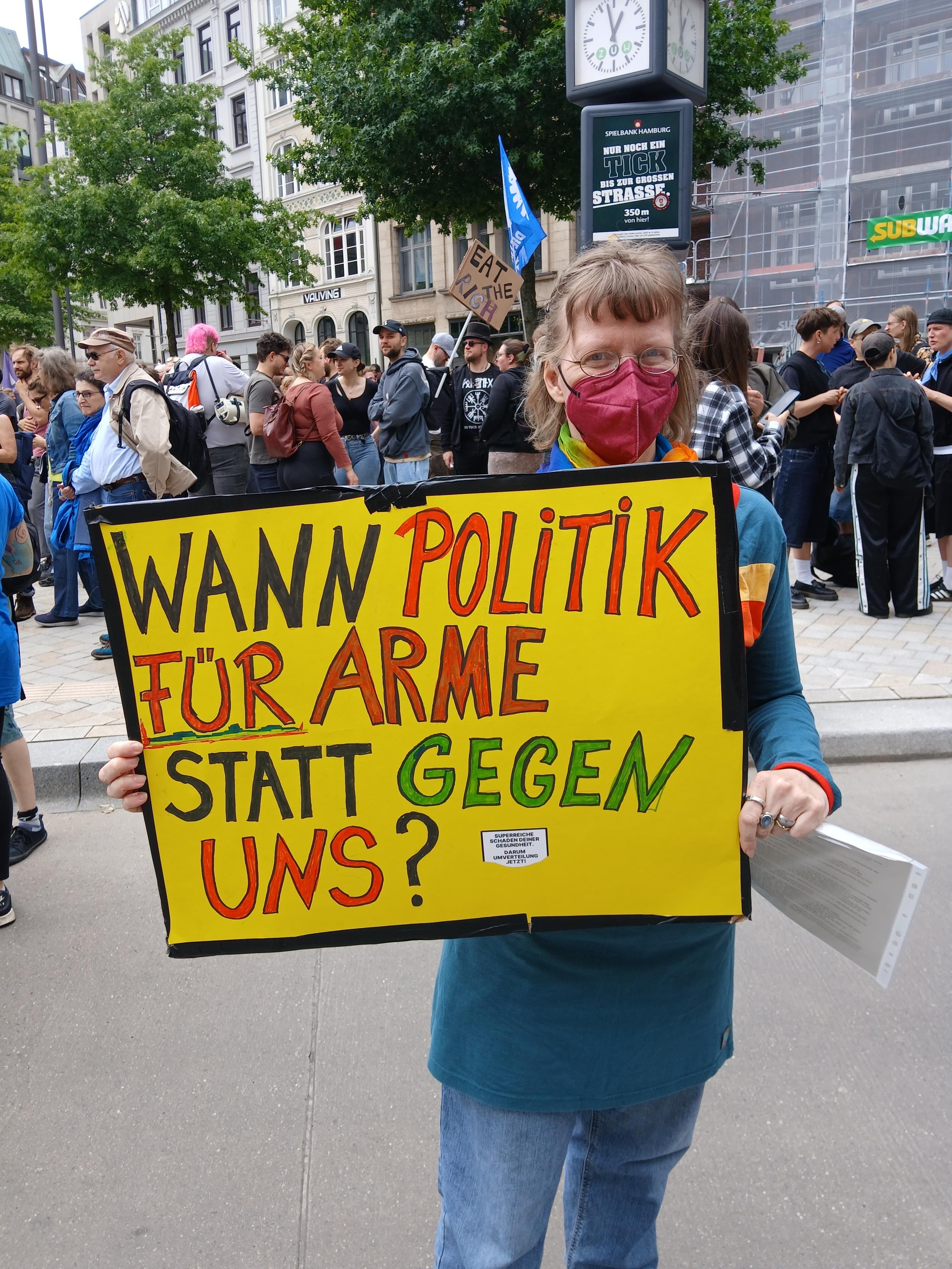 Eine Frau mit Maske und Demoschild auf dem steht: Wann Politik für Arme statt gegen uns?